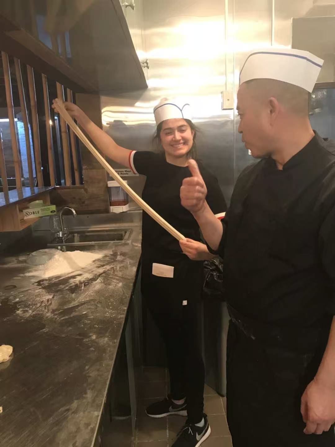 Apprentice stretching dough, master giving thumbs up