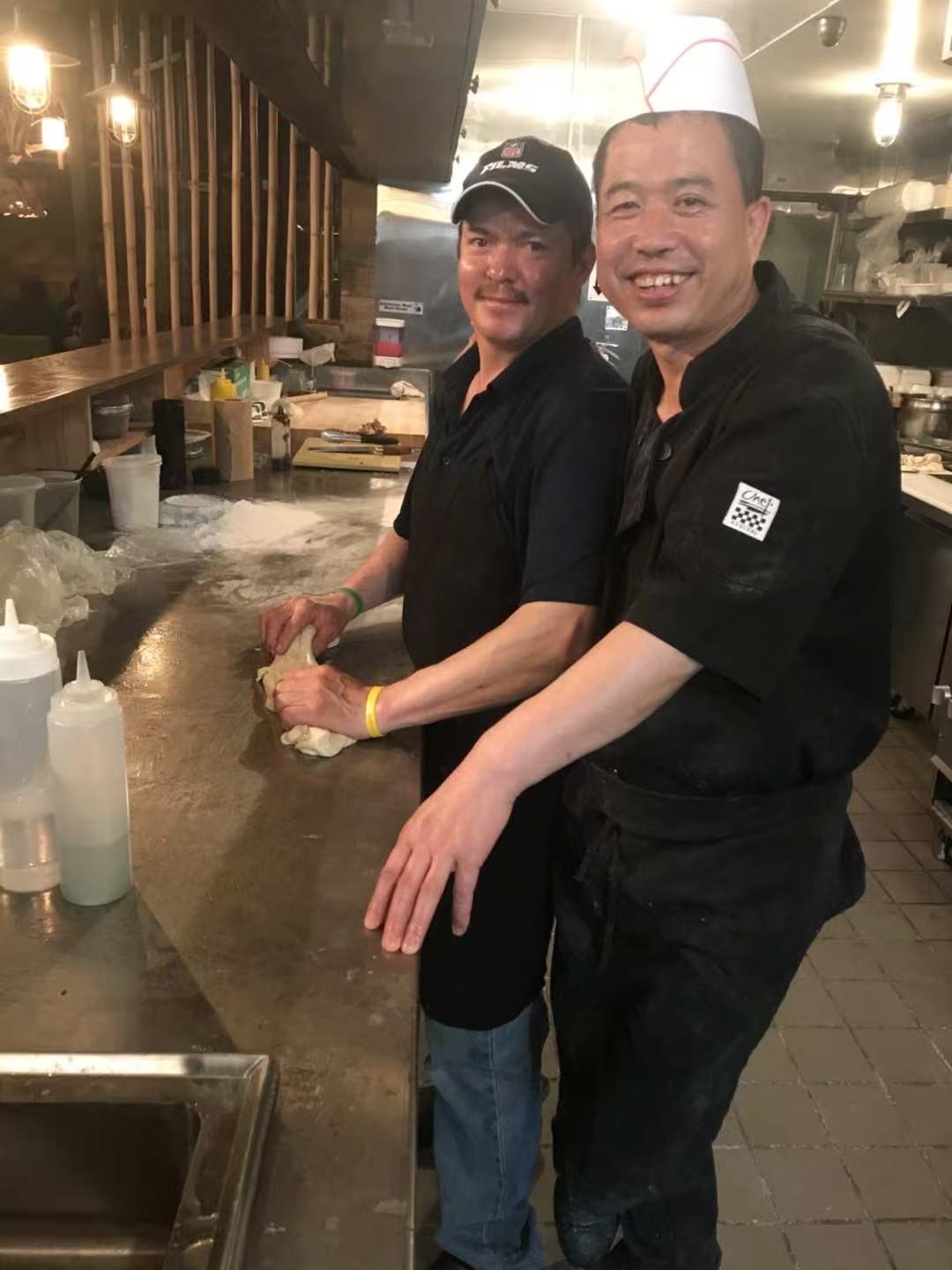Master physically guiding an apprentice's hands on the dough